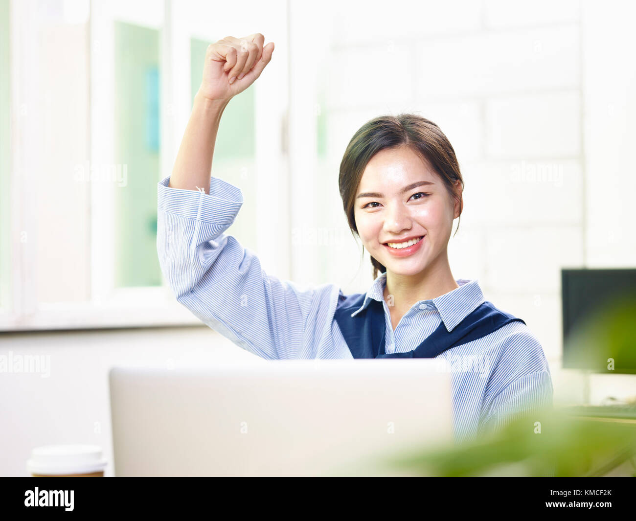 Young Asian female office worker brandissant un poing pour célébrer les succès et les réalisations. Banque D'Images