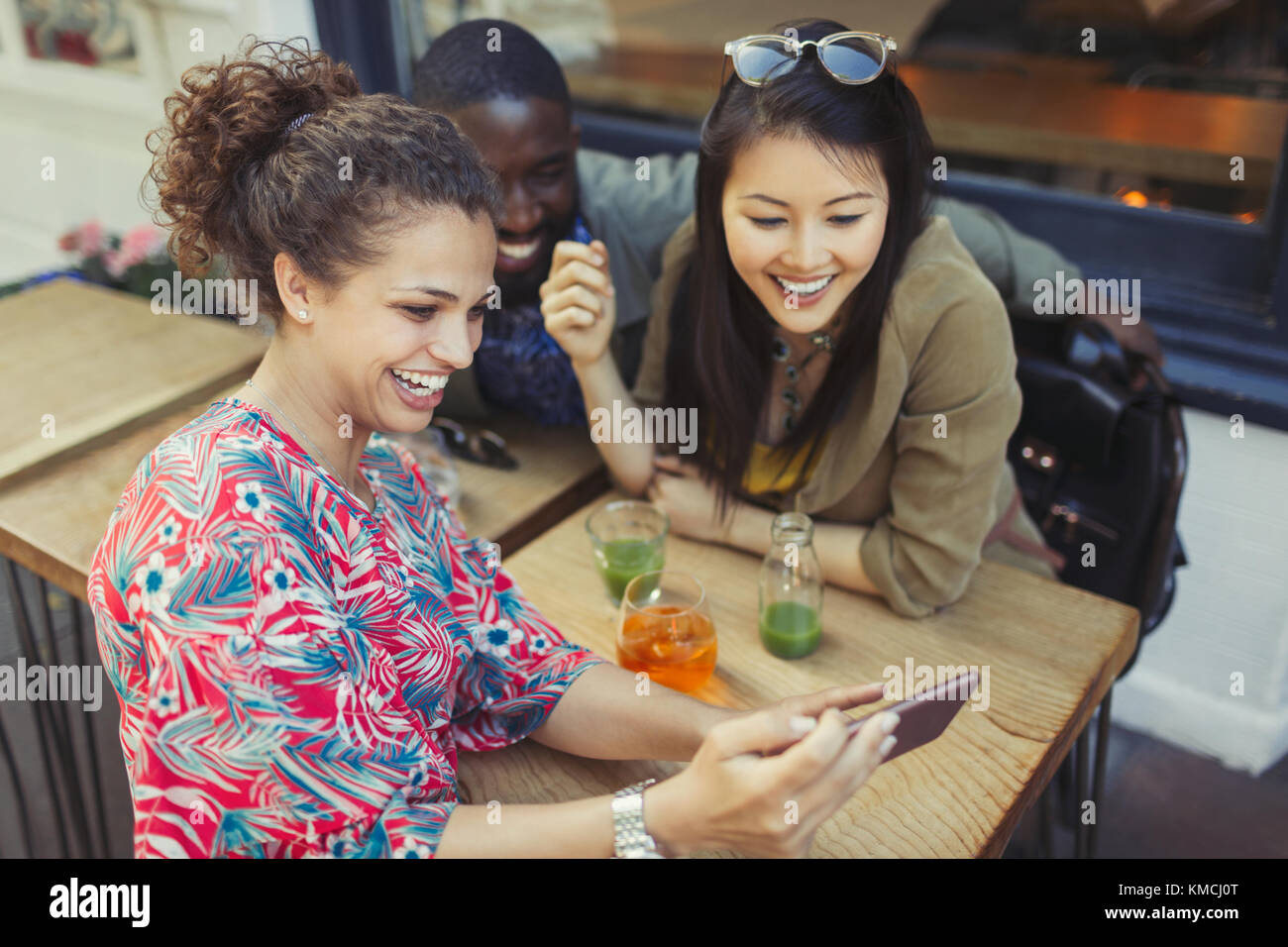 Jeunes femmes amis utilisant un téléphone intelligent au café Sidewalk Banque D'Images