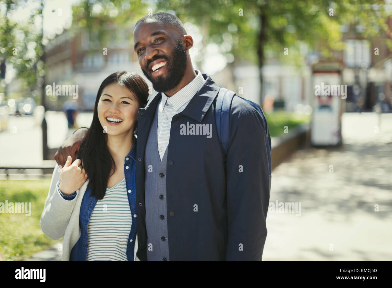 Un jeune couple souriant et affectueux qui s'enserre dans un parc urbain ensoleillé Banque D'Images