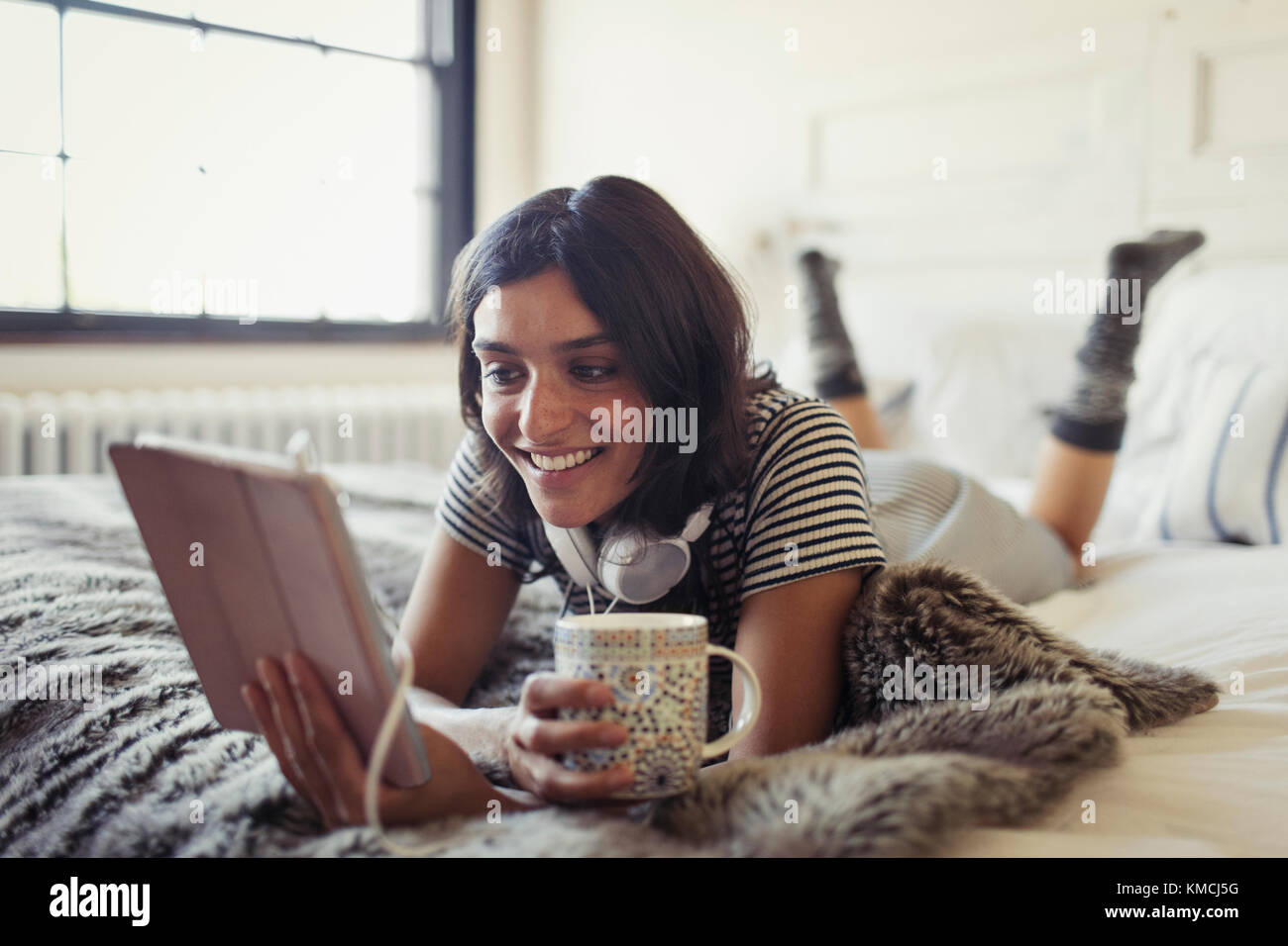 Une jeune femme souriante boit du café et utilise une tablette numérique lit Banque D'Images