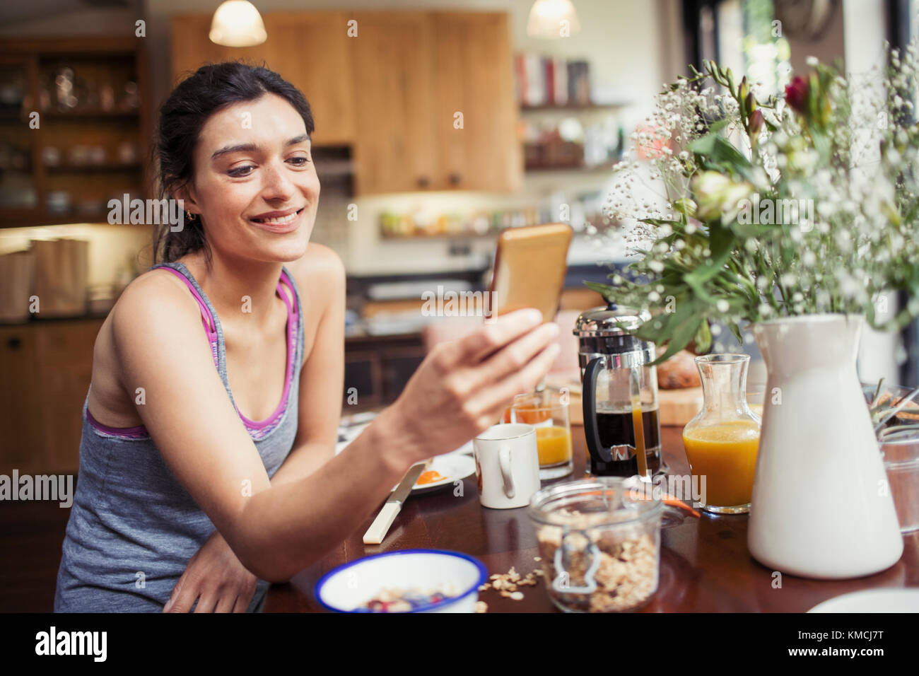 Une jeune femme souriante envoie des SMS avec un smartphone à la table du petit-déjeuner Banque D'Images