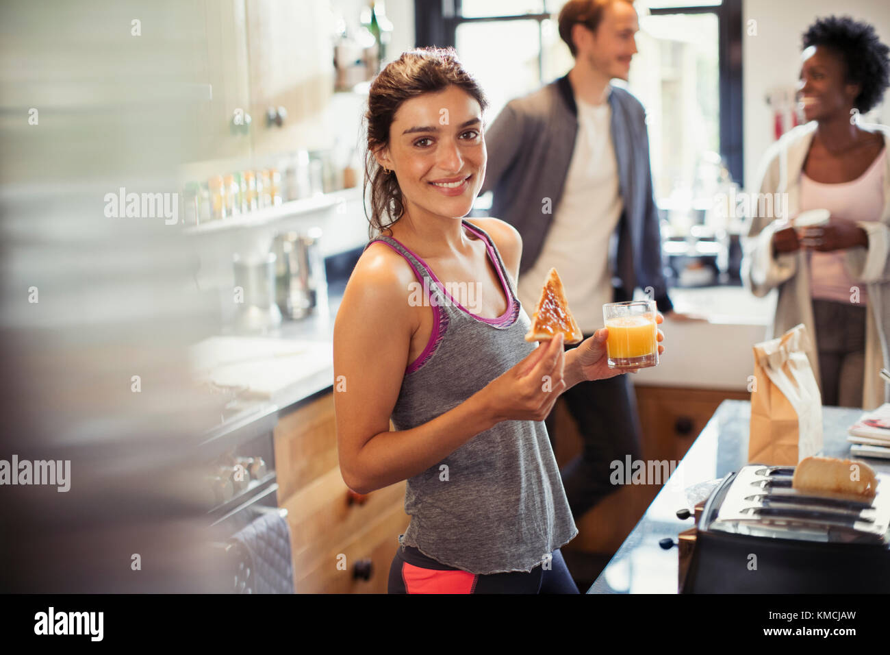 Portrait souriante jeune femme mangeant du pain grillé et buvant du jus d'orange dans la cuisine Banque D'Images