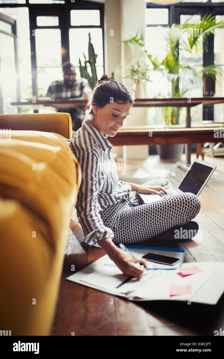 Femme indépendante travaillant à l'ordinateur portable, prenant des notes au niveau du salon Banque D'Images