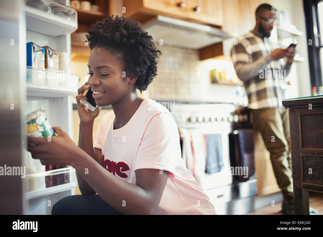 Femme parlant sur un smartphone, lisant l'étiquette sur le pot dans le réfrigérateur dans la cuisine Banque D'Images