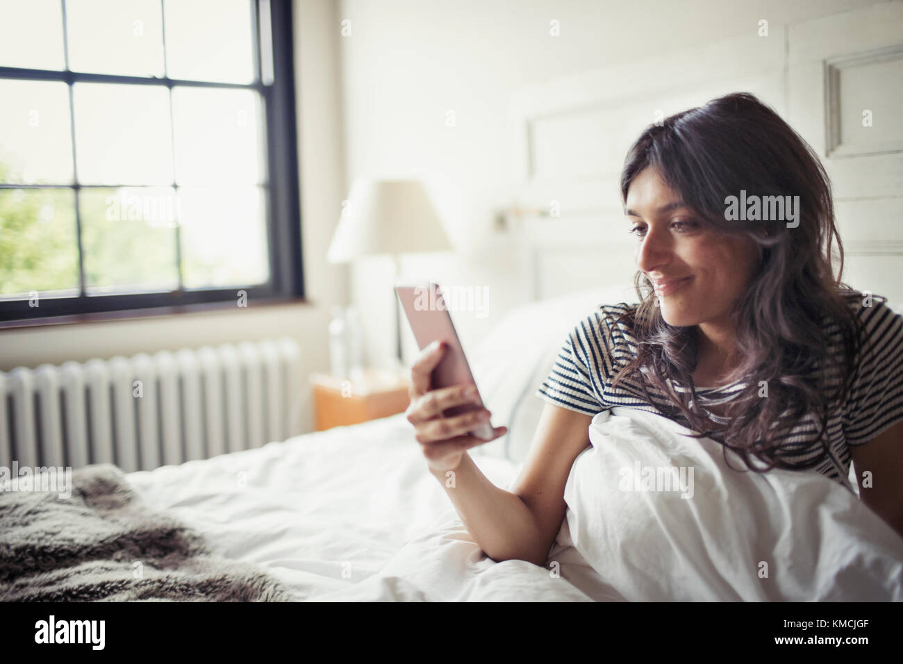 Jeune femme se détendant au lit, envoyant des SMS avec un smartphone Banque D'Images