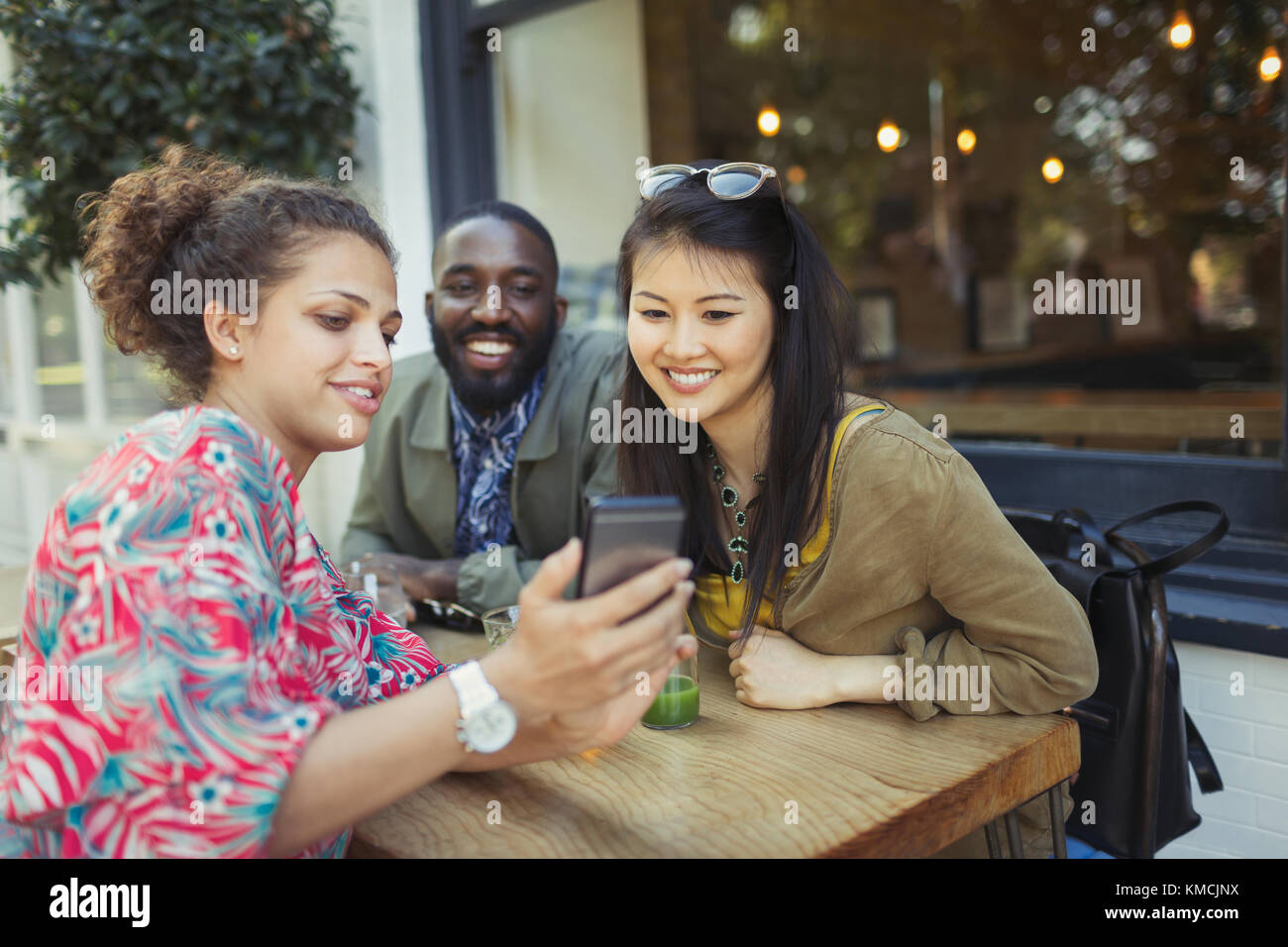 Jeunes amis utilisant un téléphone cellulaire au café-terrasse Banque D'Images