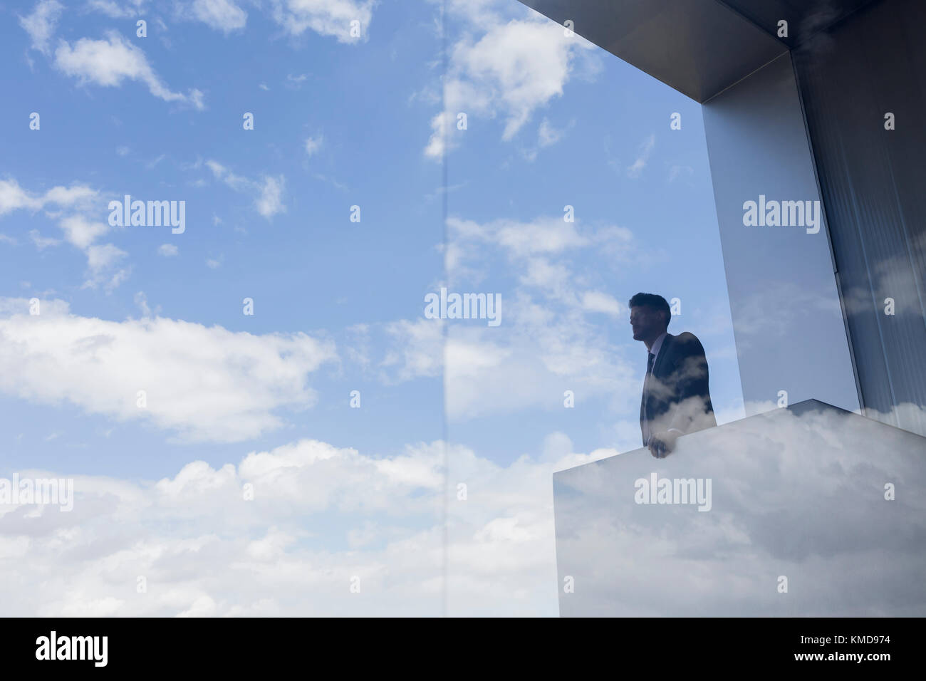 Homme d'affaires pensif sur un balcon moderne avec vue sur le ciel bleu et nuages Banque D'Images