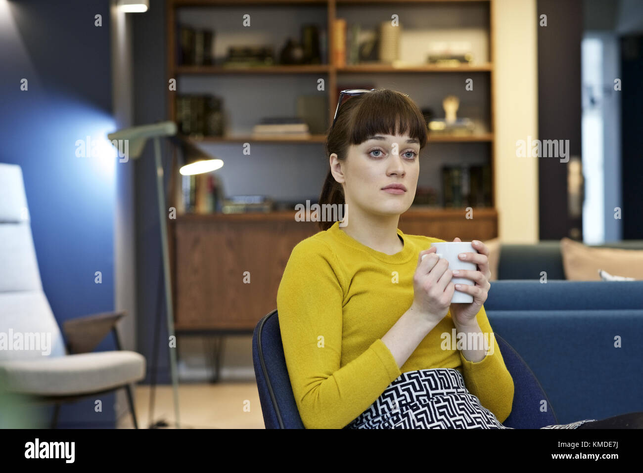 Caucasian businesswoman dans un bureau contemporain ayant une pause café avec un air pensif, contemplant Banque D'Images