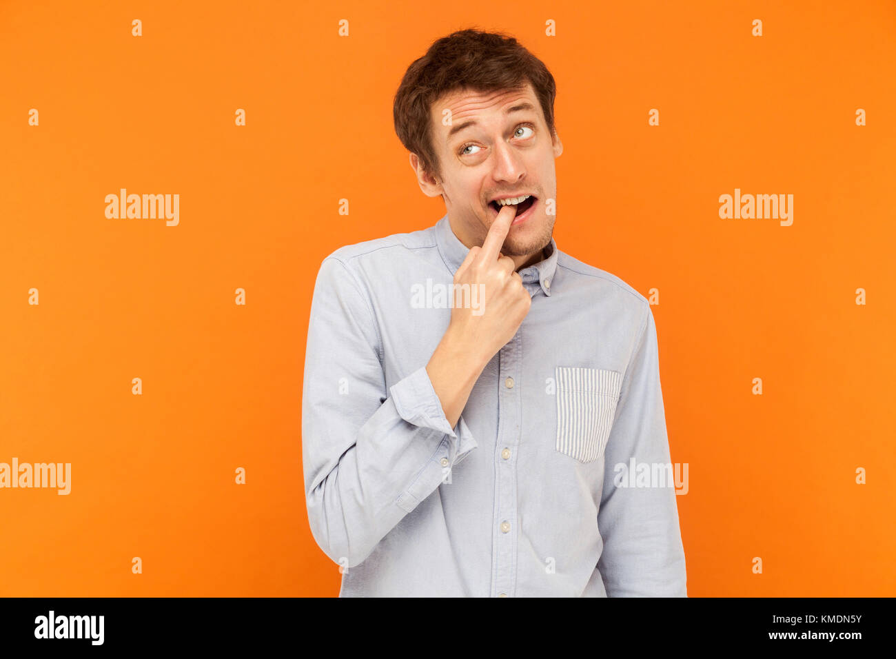 Quelque chose est coincé entre les dents. L'homme d'affaires jeune adulte  drôle de toucher les dents et doigts en haut. Fond orange, Studio shot  Photo Stock - Alamy