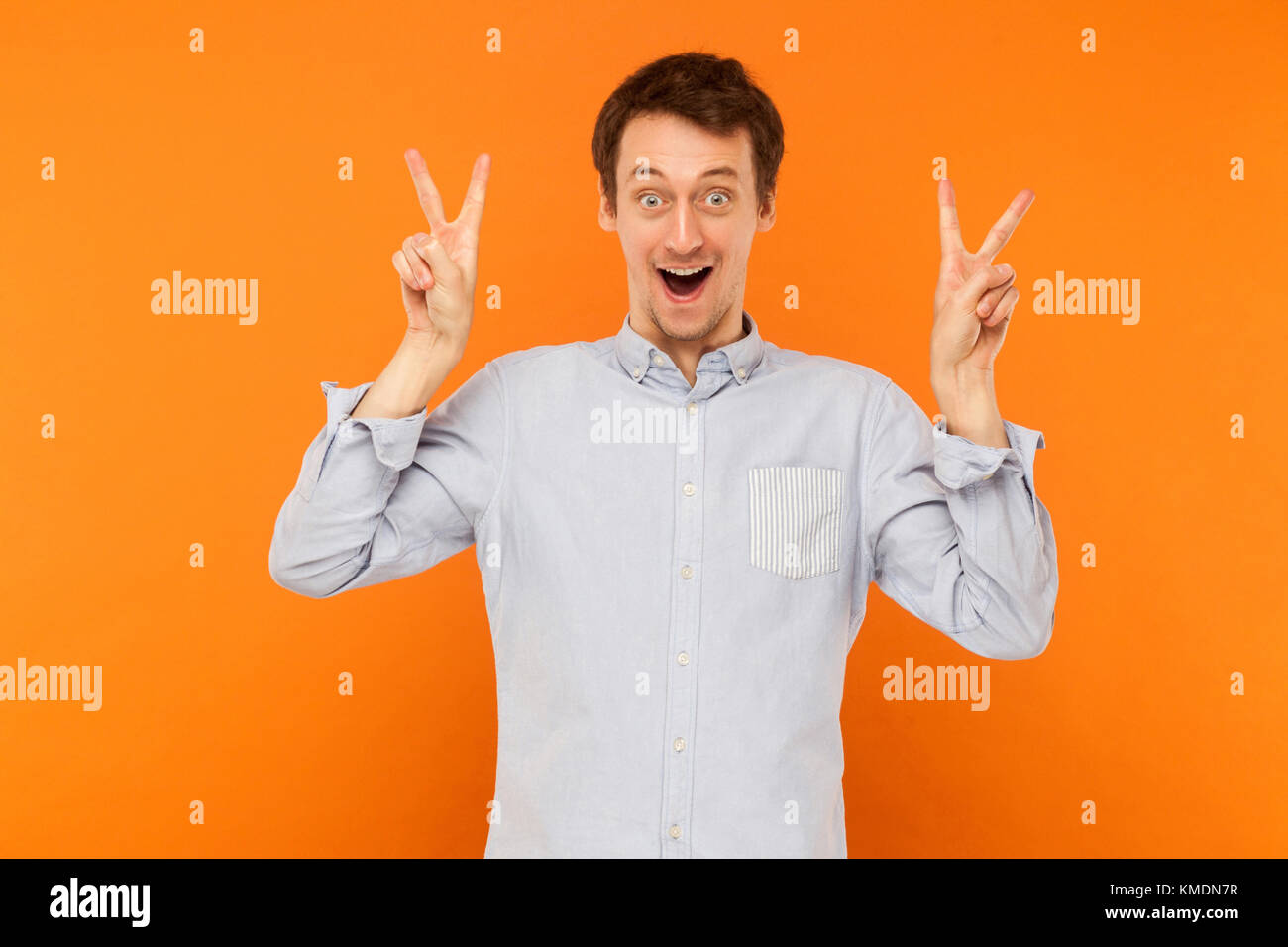 Signe de la paix. Le bonheur de l'homme jeunes adultes montrant signe de paix à l'appareil photo. Fond orange, Studio shot Banque D'Images