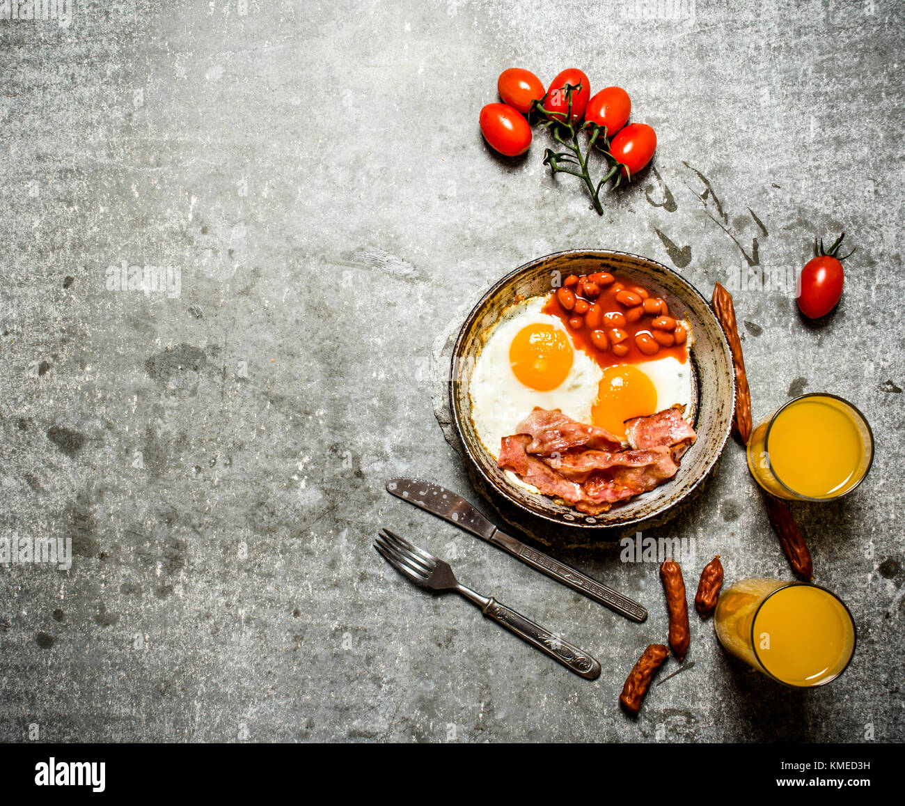 Petit-déjeuner frais. bacon avec les œufs et les haricots. jus d'orange et tomates. sur la table de pierre. Banque D'Images