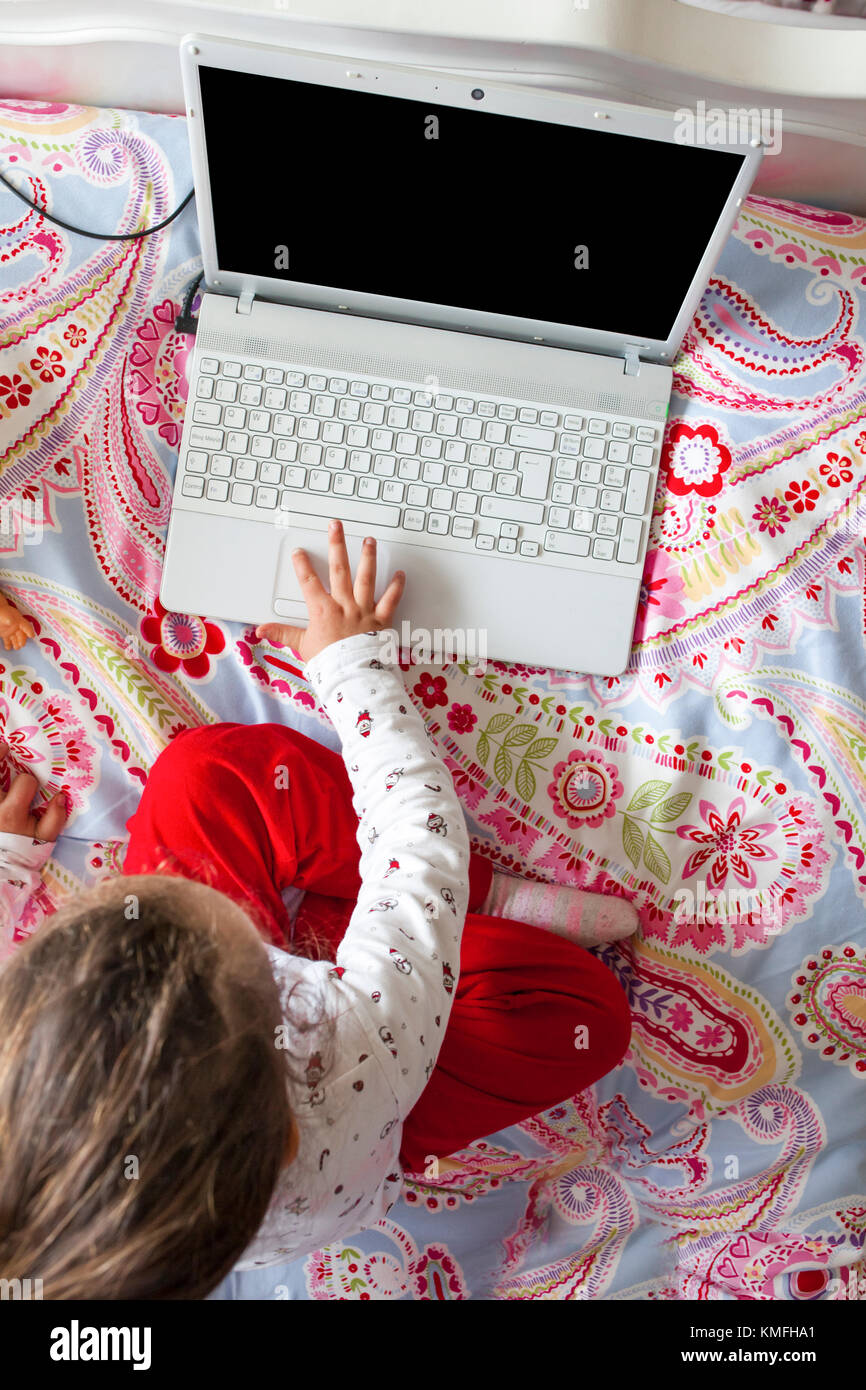 Petite fille assise dans le lit et jouer à des jeux en ligne dans sa chambre. High angle view Banque D'Images
