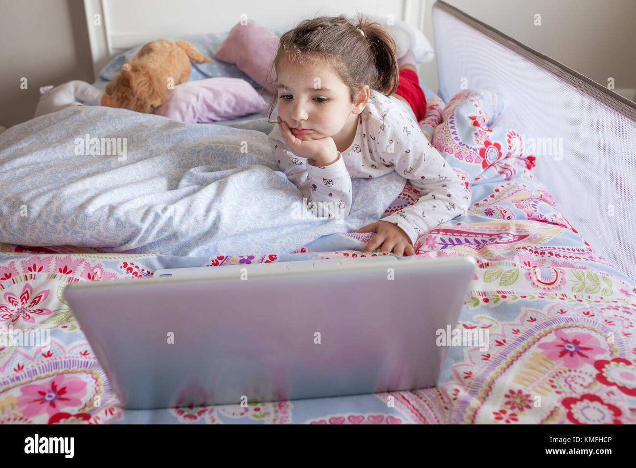 Petite fille au lit et regarder les dessins animés avec un ordinateur portable dans sa chambre. Elle a l'air amusé Banque D'Images