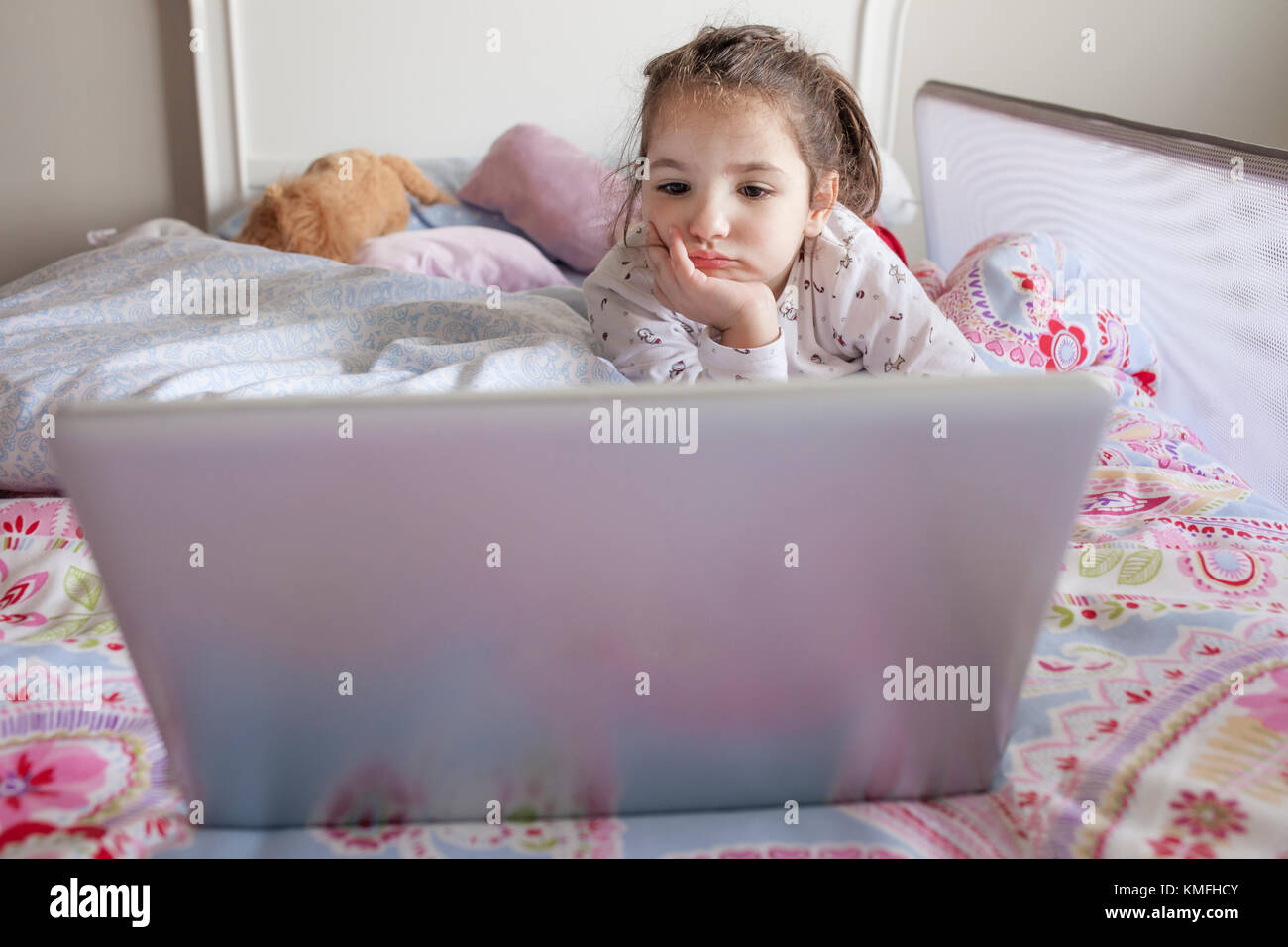 Petite fille au lit et regarder des films avec un ordinateur portable dans sa chambre. Elle a l'air ennuyé Banque D'Images