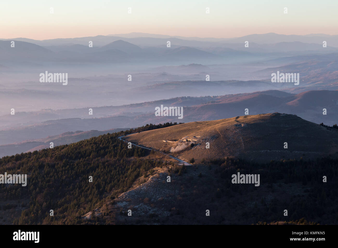 Belle vue aérienne de la montagne Subasio (Assise, Ombrie) au coucher du soleil, avec de longues ombres et couleurs chaudes, et une mer de brume remplissant la vallée ci-dessous Banque D'Images