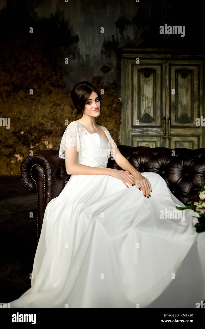 Belle robe de mariée assis sur une chaise à l'intérieur dans dark studio intérieur comme à la maison. Banque D'Images