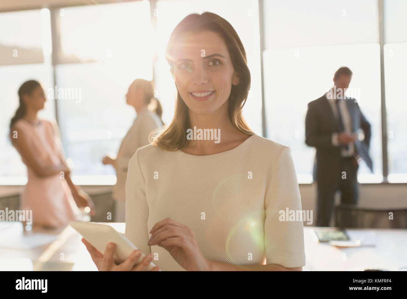 Portrait femme d'affaires souriante utilisant une tablette numérique dans un bureau ensoleillé Banque D'Images