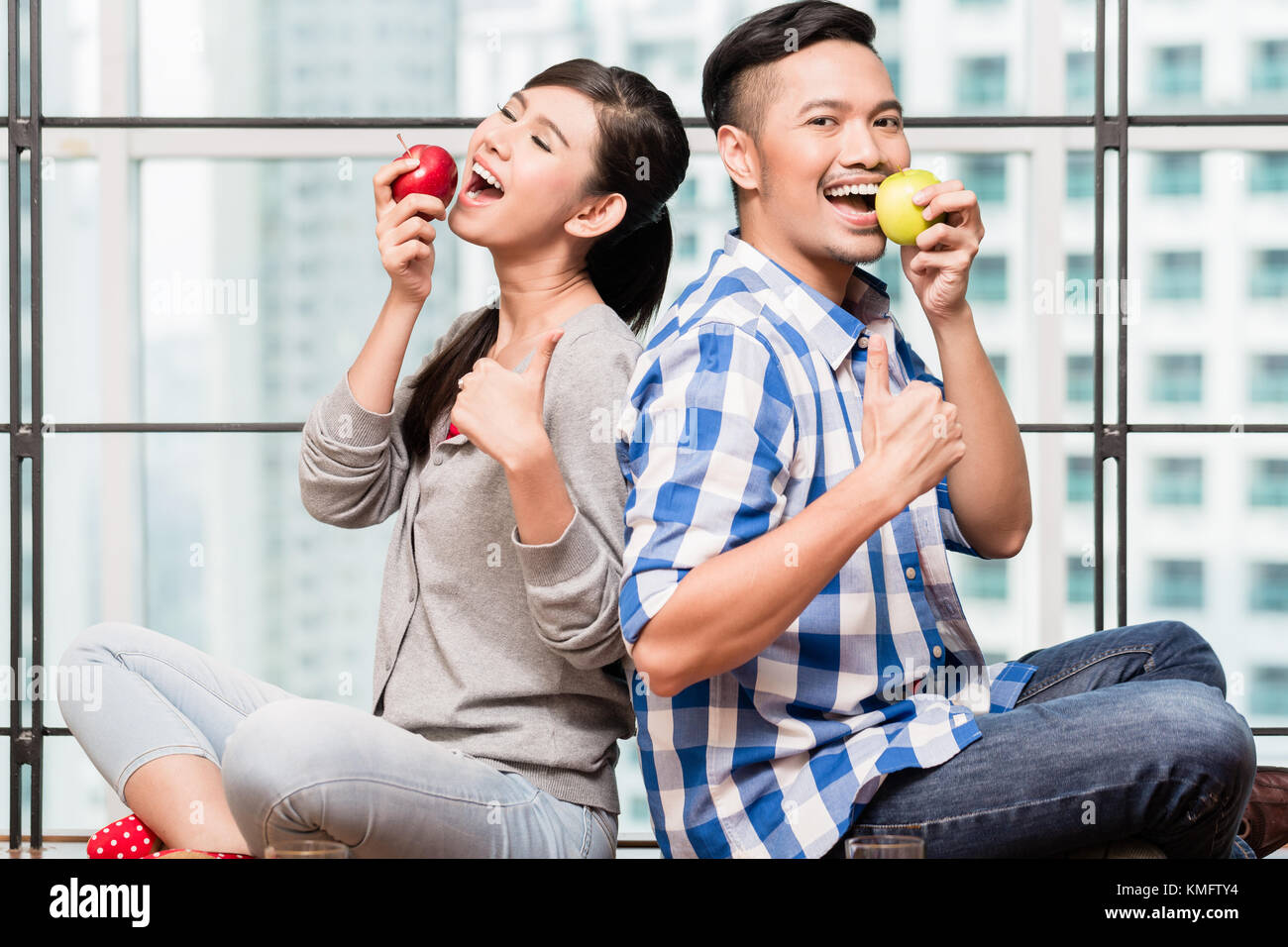Asian couple, femme et homme, ayant pommes comme collation santé dans leur télévision urbaine Banque D'Images