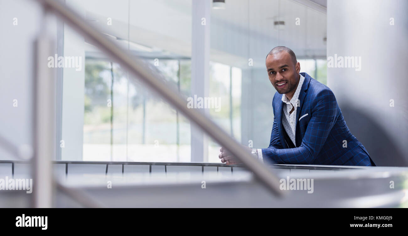 Portrait homme d'affaires souriant penché sur la rampe dans le bureau Banque D'Images