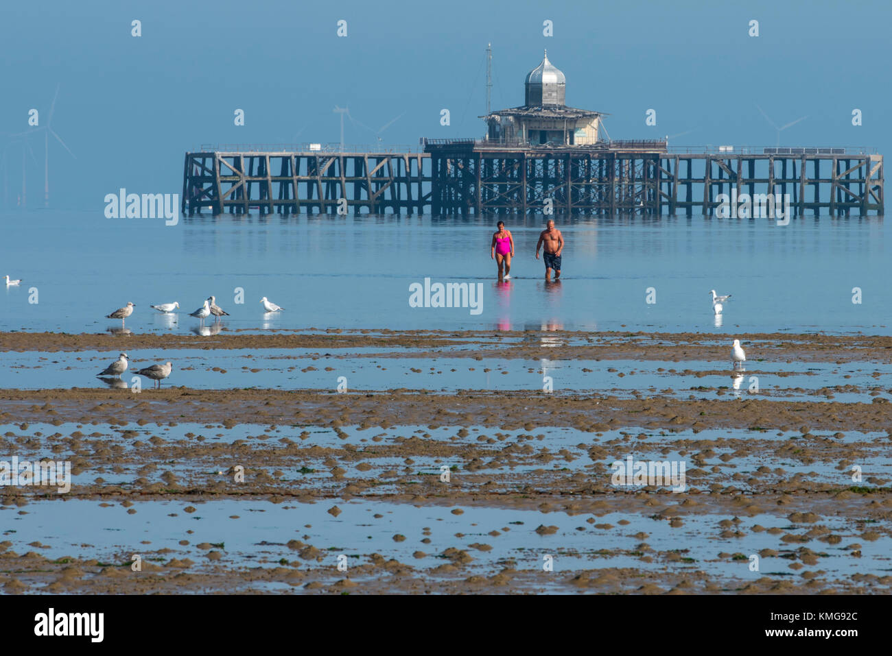 Un couple portant des maillots de marcher dans la mer Retour à la plage après avoir regardé les ruines de l'ancienne jetée à Herne Bay, Kent. Banque D'Images