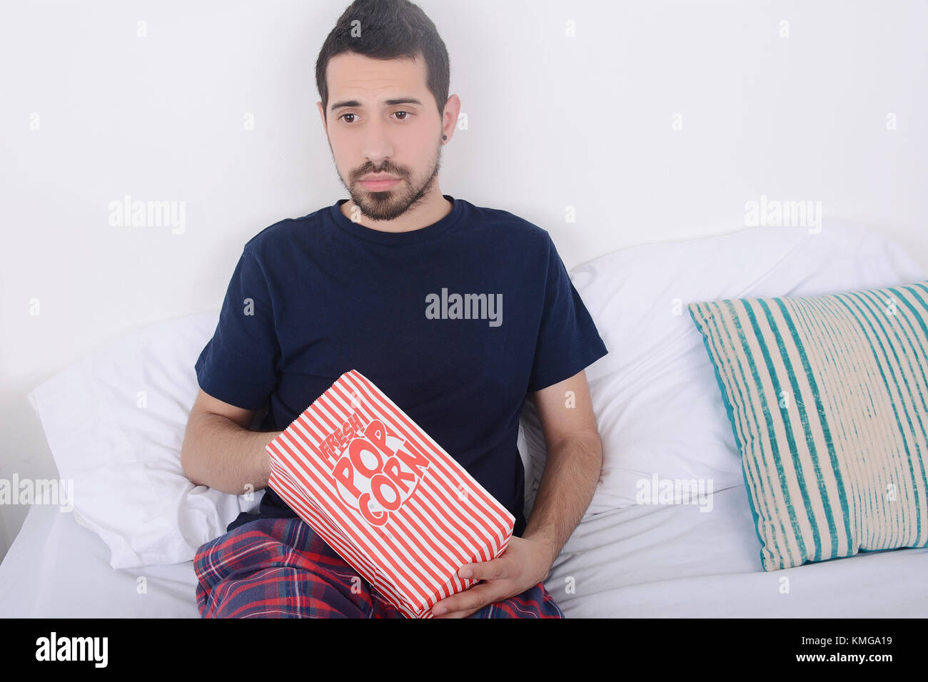 Young man eating popcorn et regarder des films détendu sur lit. à l'intérieur. Banque D'Images