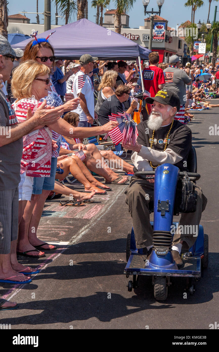 Équitation son fauteuil roulant motorisé sur la rue principale, un vétéran de la guerre du vietnam la foule avec des cadeaux gratuitement des drapeaux américains à un défilé du 4 juillet à Huntington Beach, ca. Banque D'Images