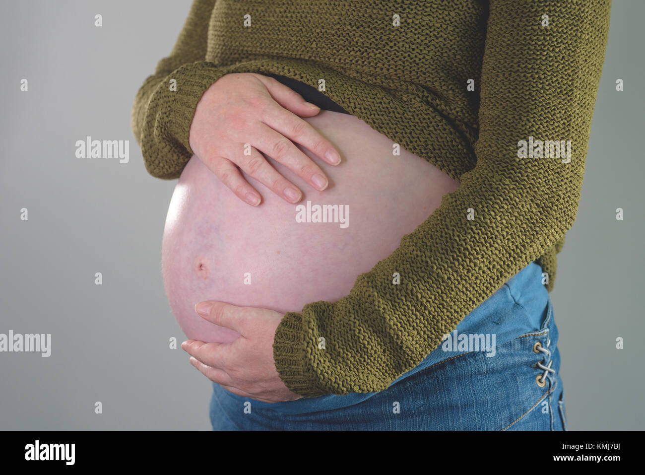 Close-up of pregnant woman with hands over ventre sur fond gris clair Banque D'Images