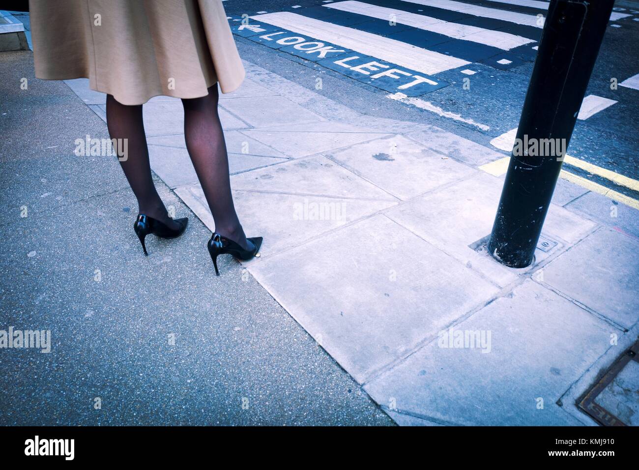 Close-up des jambes d'une femme vêtue à la mode avec un manteau, bas noirs  et des talons hauts dans la rue à côté de passage pour piétons. Londres  Photo Stock - Alamy