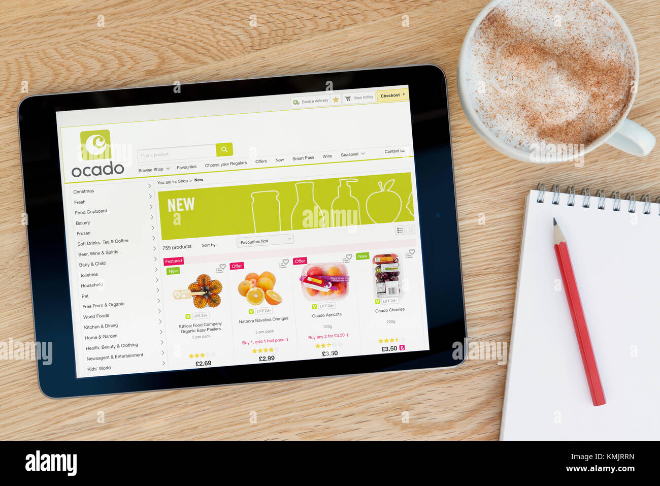 Le site web de l'Ocado dispose sur un iPad tablet device qui repose sur une table en bois à côté d'un bloc-notes et un crayon et une tasse de café (rédaction uniquement) Banque D'Images