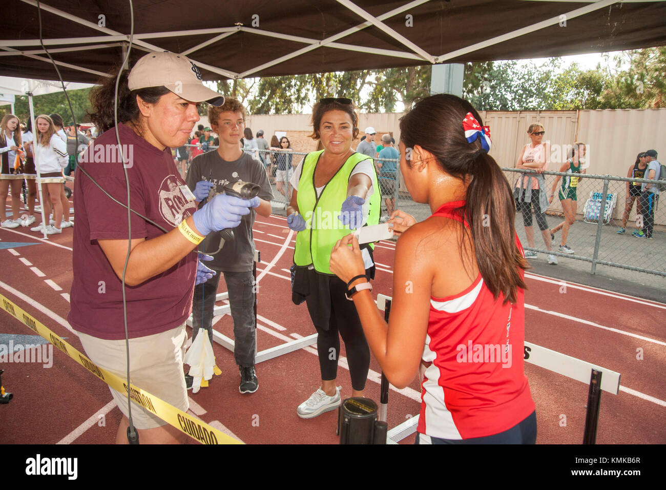 Un parent bénévole scanne le code barres de l'onglet identification de une fille de l'adolescence athlète après franchissement de la ligne d'arrivée d'une école secondaire sur invitation de cross country course à pied dans la région de Laguna Hills, ca. Le code à barres est utilisé pour déterminer son temps de marche. Banque D'Images