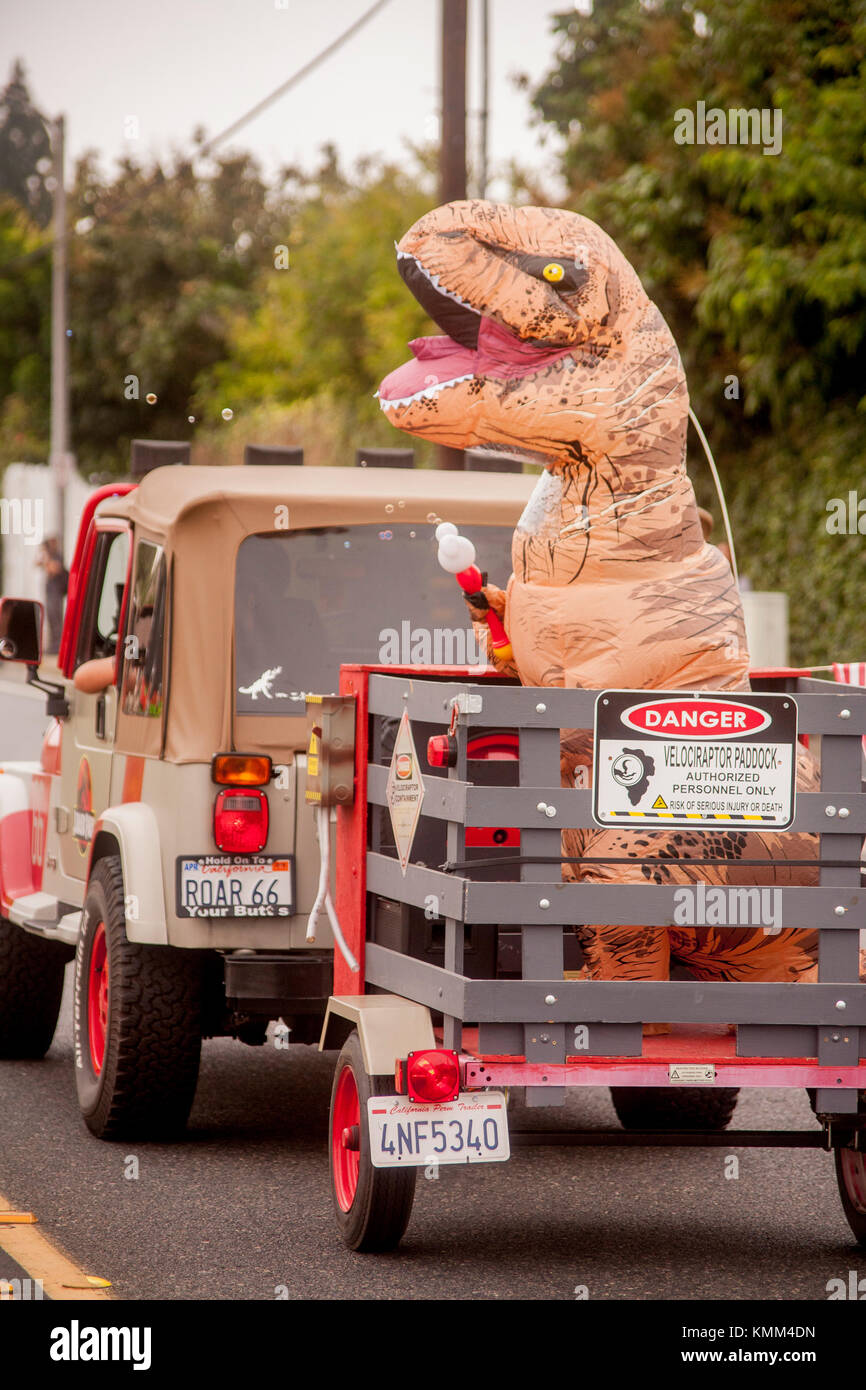 Un monstre jurassique costumés obtient un tour dans une remorque derrière une jeep dans un défilé anniversaire de la ville de Fountain Valley, ca. Remarque 'roar 66' plaque d'immatriculation. Banque D'Images