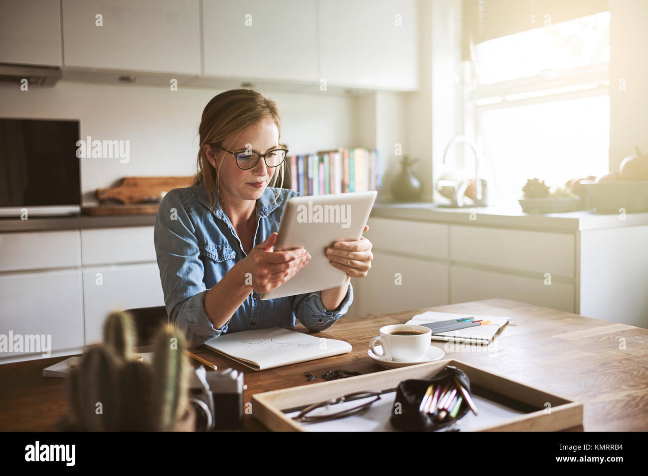 Jeune femme assise à sa table de cuisine à la maison de travailler sur sa petite entreprise avec une tablette numérique Banque D'Images