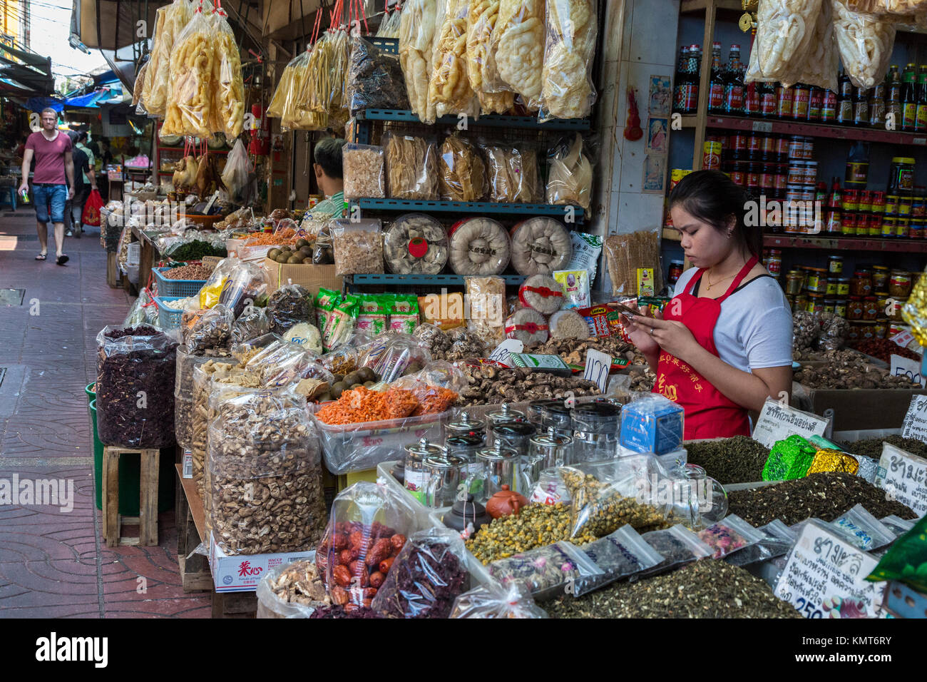 Bangkok, Thaïlande. Jeune femme à l'aide de son téléphone portable dans une boutique dans le marché des aliments chinois, Chinatown. Banque D'Images