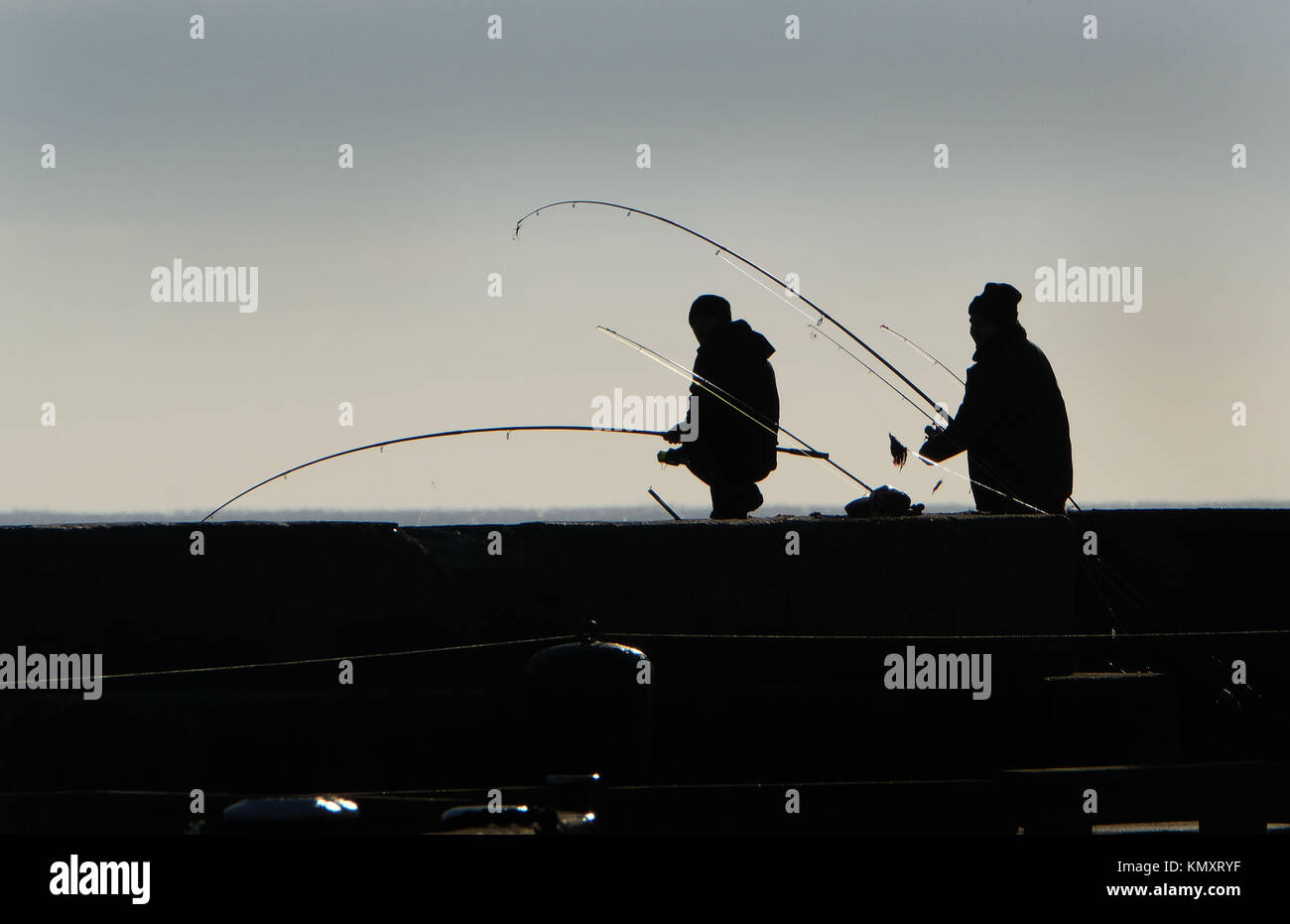 Deux hommes pêche en mer à partir de la station pier en silhouette. Banque D'Images