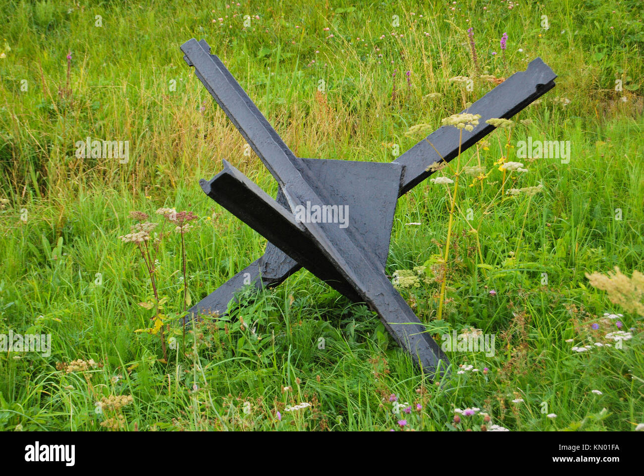 Un hérisson antichars noir de la guerre se tient sur l'herbe verte. Le concept de la guerre et de la paix. Banque D'Images