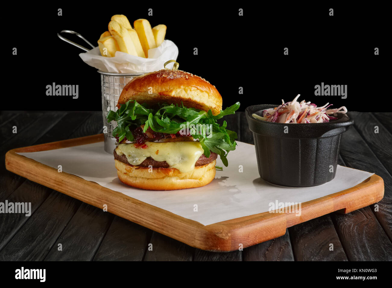 Burger de boeuf juteux avec sauce aux airelles, de fromage fondu, la roquette, servi avec du chou rouge et de pommes de terre frites Banque D'Images
