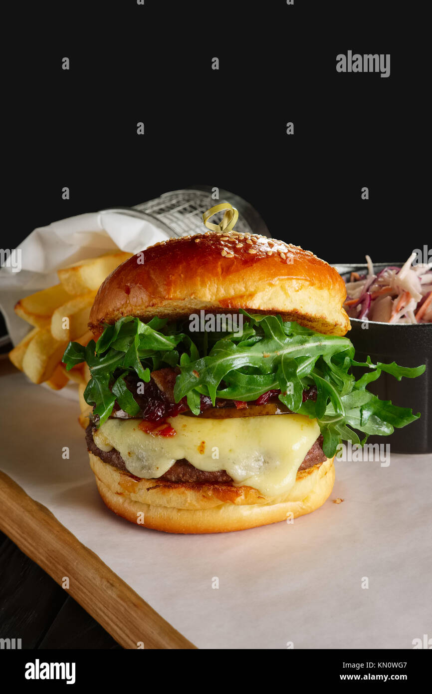 Burger de boeuf juteux avec sauce aux airelles, de fromage fondu, la roquette, servi avec du chou rouge et de pommes de terre frites Banque D'Images