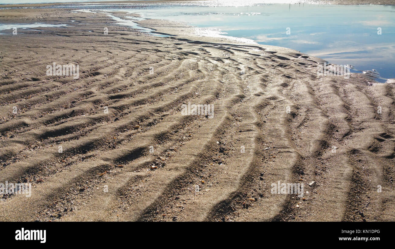 Ondulations dans le sable avec des reflets du ciel dans l'eau. Banque D'Images