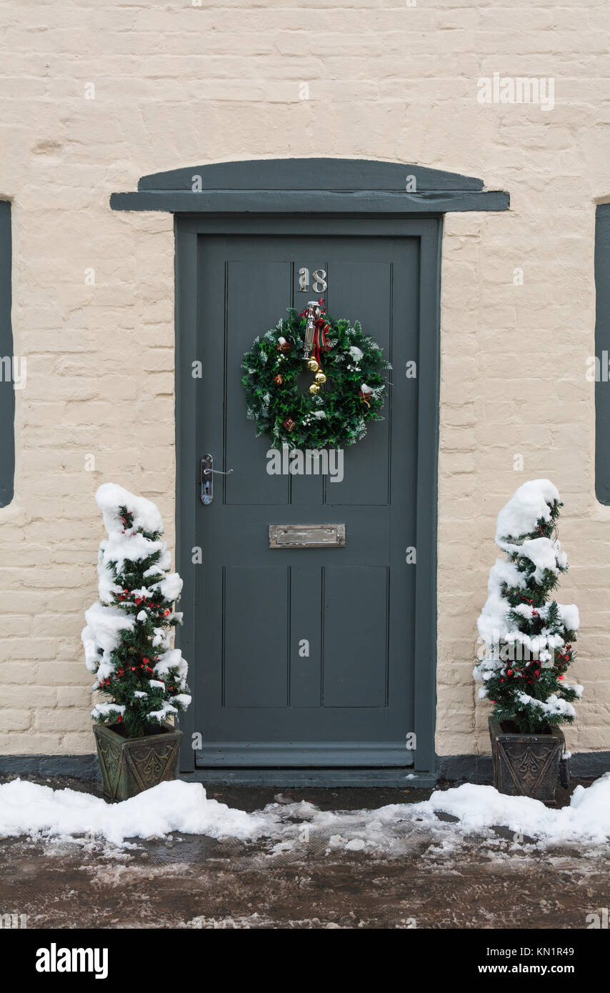 Porte d'un chalet, après une tempête de neige, avec décoration de Noël et deux arbres de Noël miniature de chaque côté, Much Wenlock, Shropshire, au Royaume-Uni. Banque D'Images