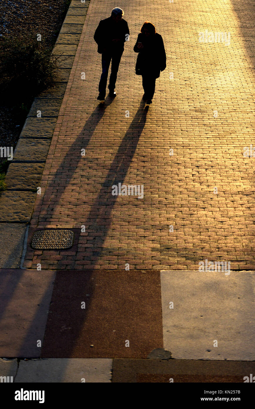 Couple en train de marcher le long d'un trottoir casting long hiver ombres, Banque D'Images