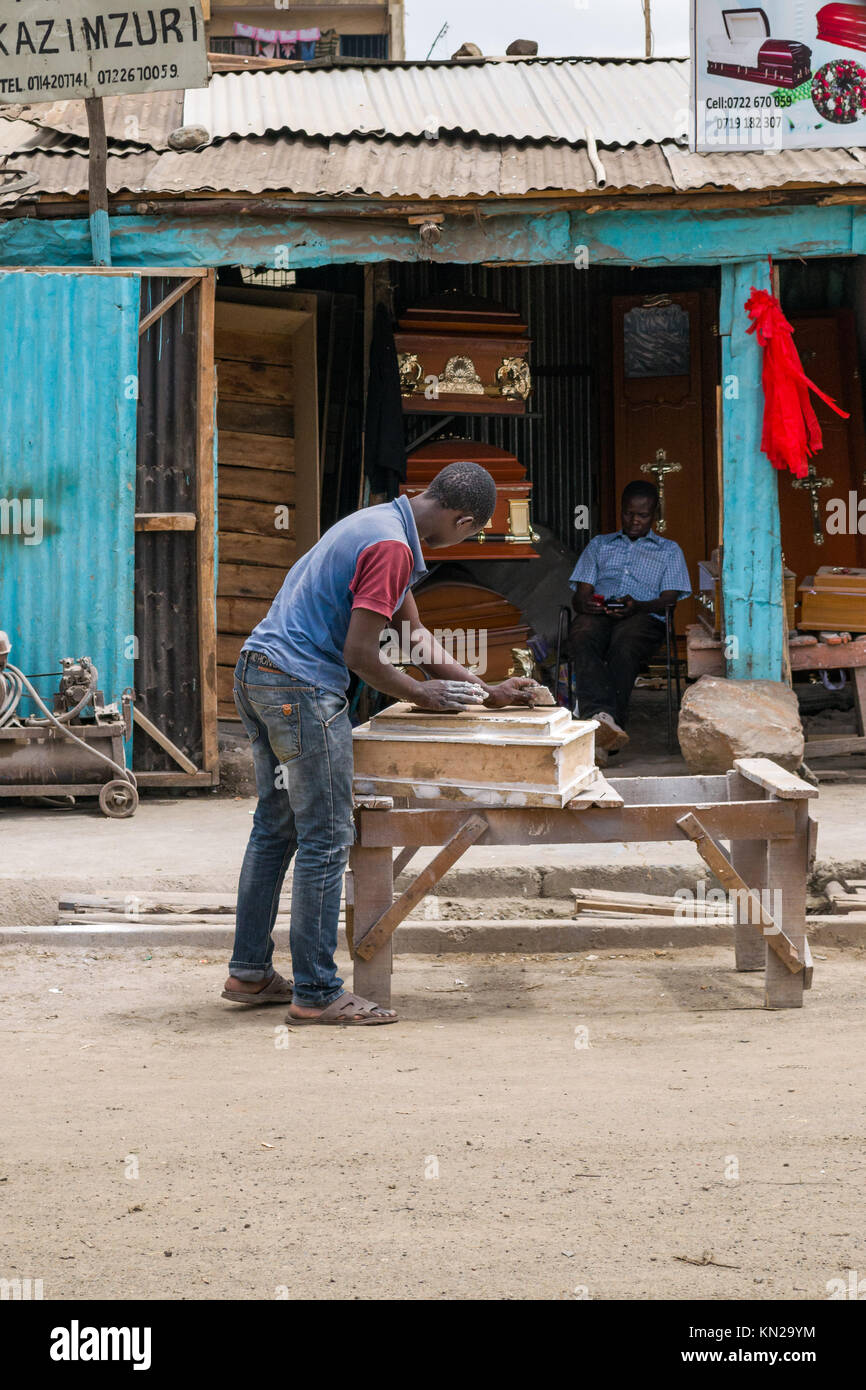 Un jeune homme kenyan travaillant sur la route d'un petit cercueil d'enfant à partir de bois et autres matériaux à l'extérieur de la boutique, Huruma, Nairobi, Kenya, E Banque D'Images