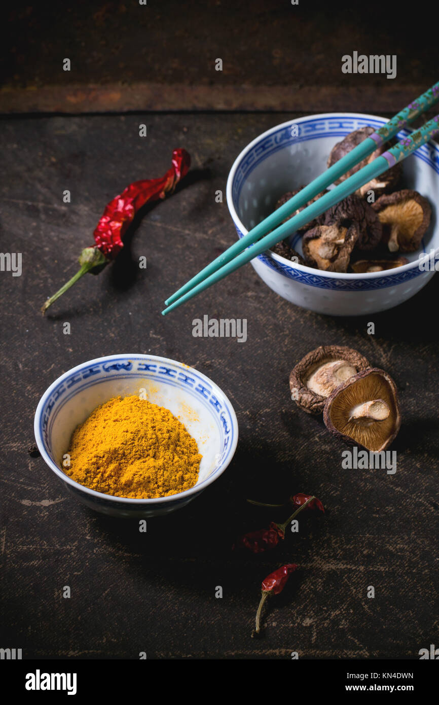 Curcuma poudre et les champignons shiitake dans des bols en porcelaine, servi avec Red Hot Chili Peppers et baguettes turquoise foncé sur table. Voir la série Banque D'Images