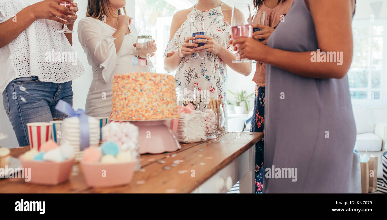 Cropped shot de gâteau et sucrés sur table avec des femmes debout autour d'un verre dans la partie de douche de bébé. Female friends enjoying partie de douche de bébé Banque D'Images