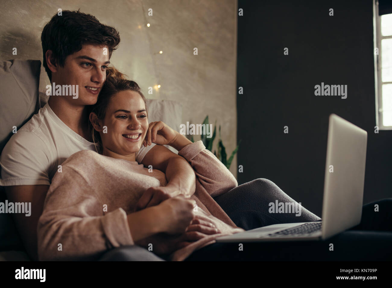 Hygge couple avec ordinateur portable sur lit. L'homme et la femme en regardant la vidéo sur ordinateur portable tout en vous relaxant dans la chambre. Banque D'Images
