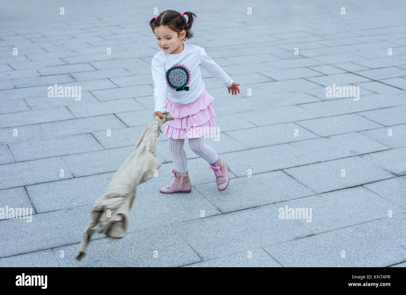 Heureux trois ans, fille jouant avec son manteau dans la ville. Focus sélectif. Banque D'Images