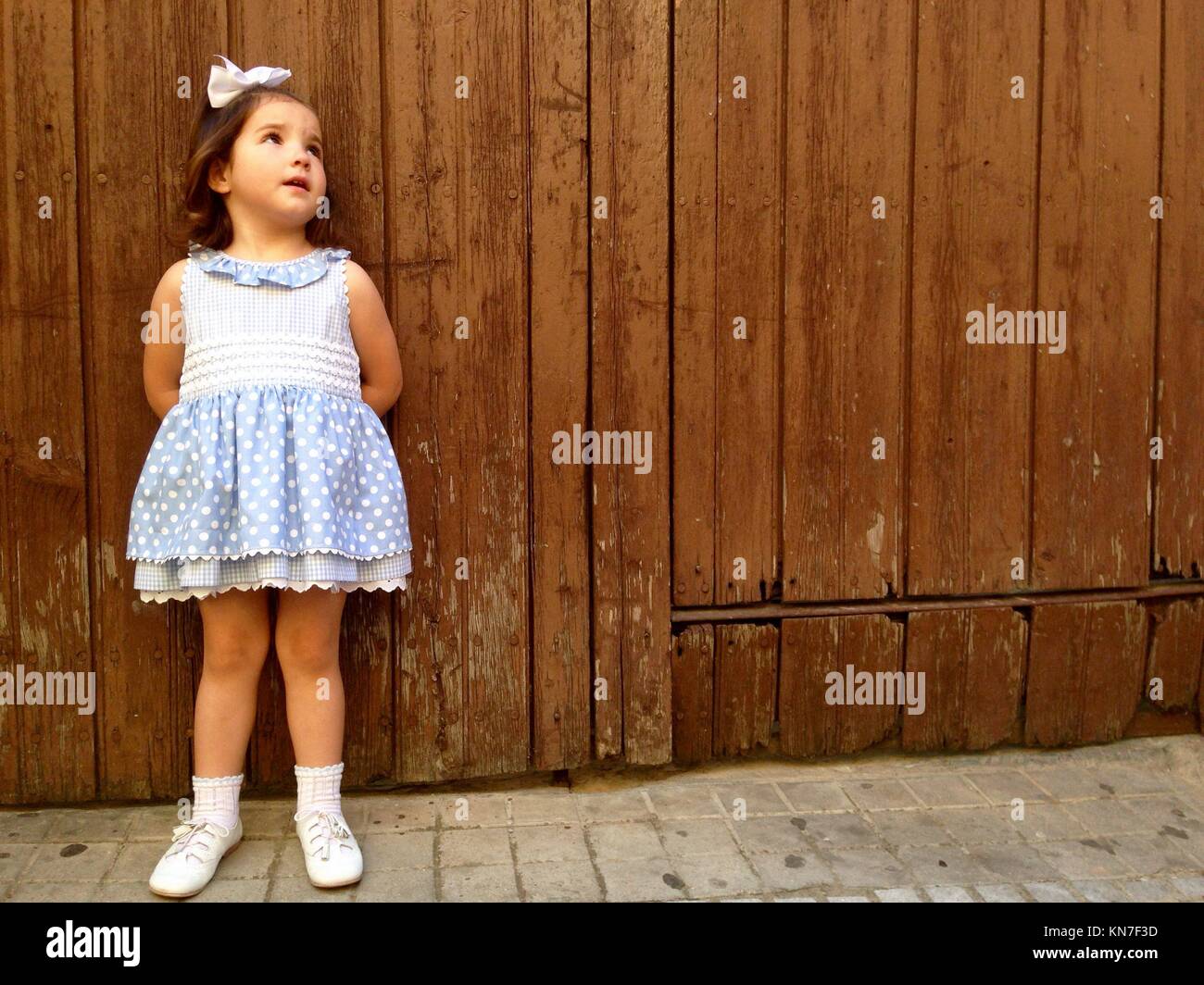 Jolie petite fille rêveur debout au-dessus de porte en bois patiné avec robe d'été. Banque D'Images