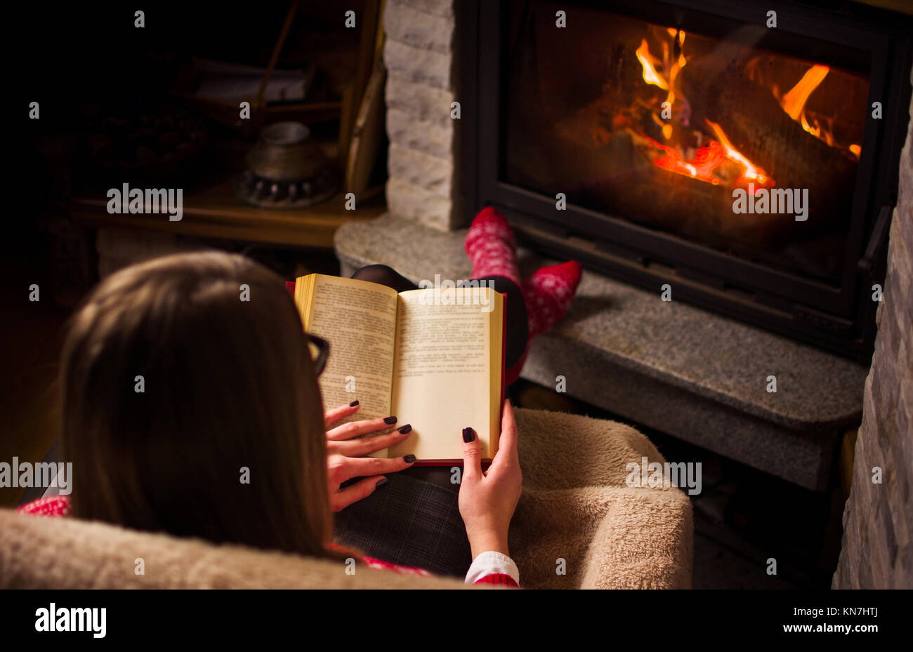 Femme lisant un livre près de la cheminée. Vie d'hiver douillet Banque D'Images