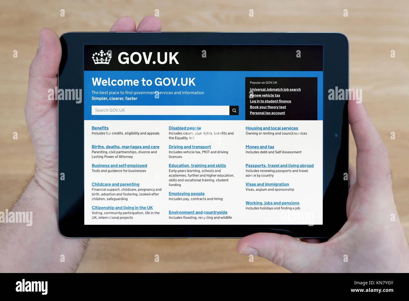 Un homme regarde le Gov.UK site sur son iPad tablet device, tourné contre une table en bois page contexte (usage éditorial uniquement) Banque D'Images