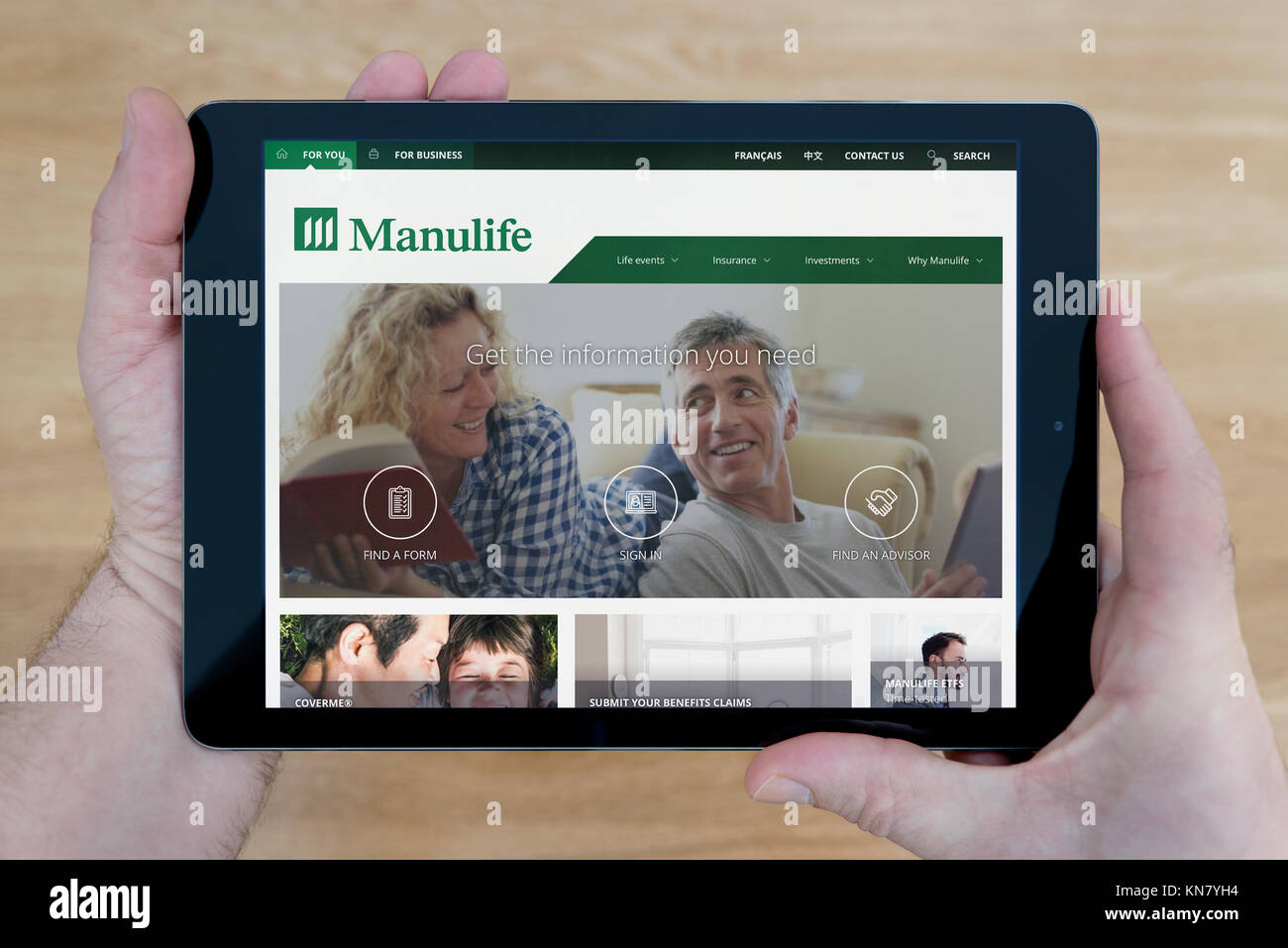 Un homme regarde le site web de Manuvie sur son iPad tablet device, tourné contre une table en bois page contexte (usage éditorial uniquement) Banque D'Images