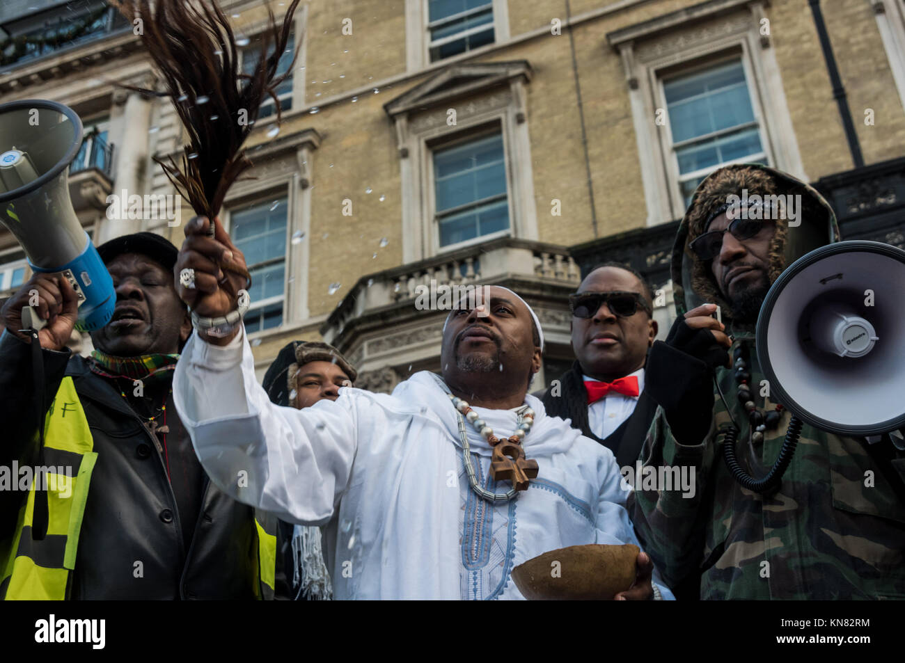 9 décembre 2017 - Londres, Royaume-Uni. 9 décembre 2017. Un homme en robe blanche termine une cérémonie de libation africaine en l'honneur des héros des luttes africaines en jetant de l'eau sur la foule lors de la manifestation devant l'ambassade libyenne contre la vente d'Africains noirs par des marchands d'esclaves arabes en Libye. La marche organisée par African Lives Matter a exigé la fermeture des centres de détention libyens, l’action des gouvernements africains pour secourir les personnes détenues dans les camps et la condamnation de la traite des esclaves et des meurtres de migrants par tous les dirigeants africains et l’ONU, appelant la Libye à faire et à faire appliquer des lois en ce sens Banque D'Images